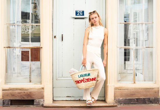 Frau steht im Türrahmen mitten in St. Tropez und trägt eine Basttasche von Liqueur Tropézienne