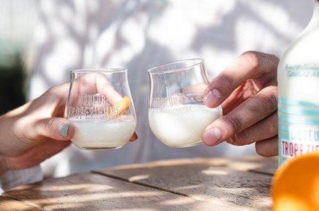 Man and woman sitting in a beach club on the Plage Pampelonne toasting each other with Liqueur Tropézienne