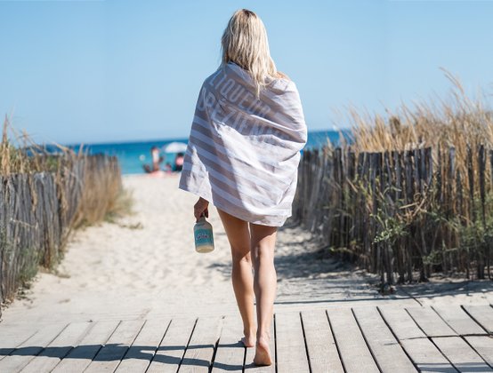 Frau läuft auf Steg am Plage Pampelonne entlang und führt ihr Bohème Strandtuch von Liqueur Tropézienne vor